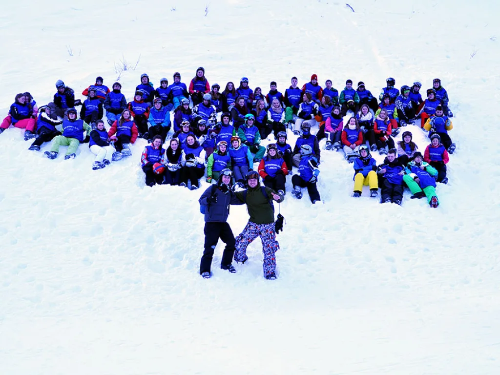Große Gruppe hat sich zu einer Figur im Schnee aufgestellt.